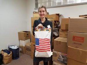 Olga holding a bag of clothes that will be donated to Ukraine. There is an American flag printed on the bag.