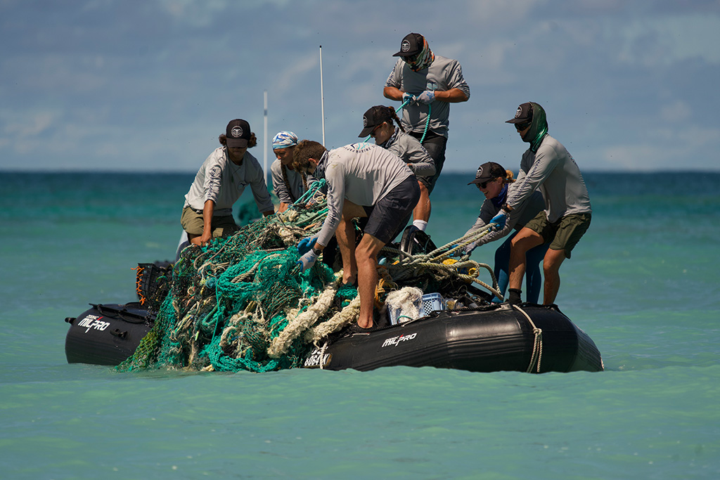 7 people hauling a large bundle of derelict fishing nets onto a Zodiac boat