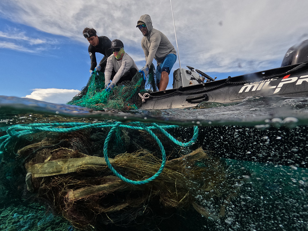 3 crew members hauling derelict fishing nets out of the ocean and onto a Zodiac boat