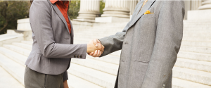 A woman wearing a business suit shaking hands with a man who is wearing a business suit.