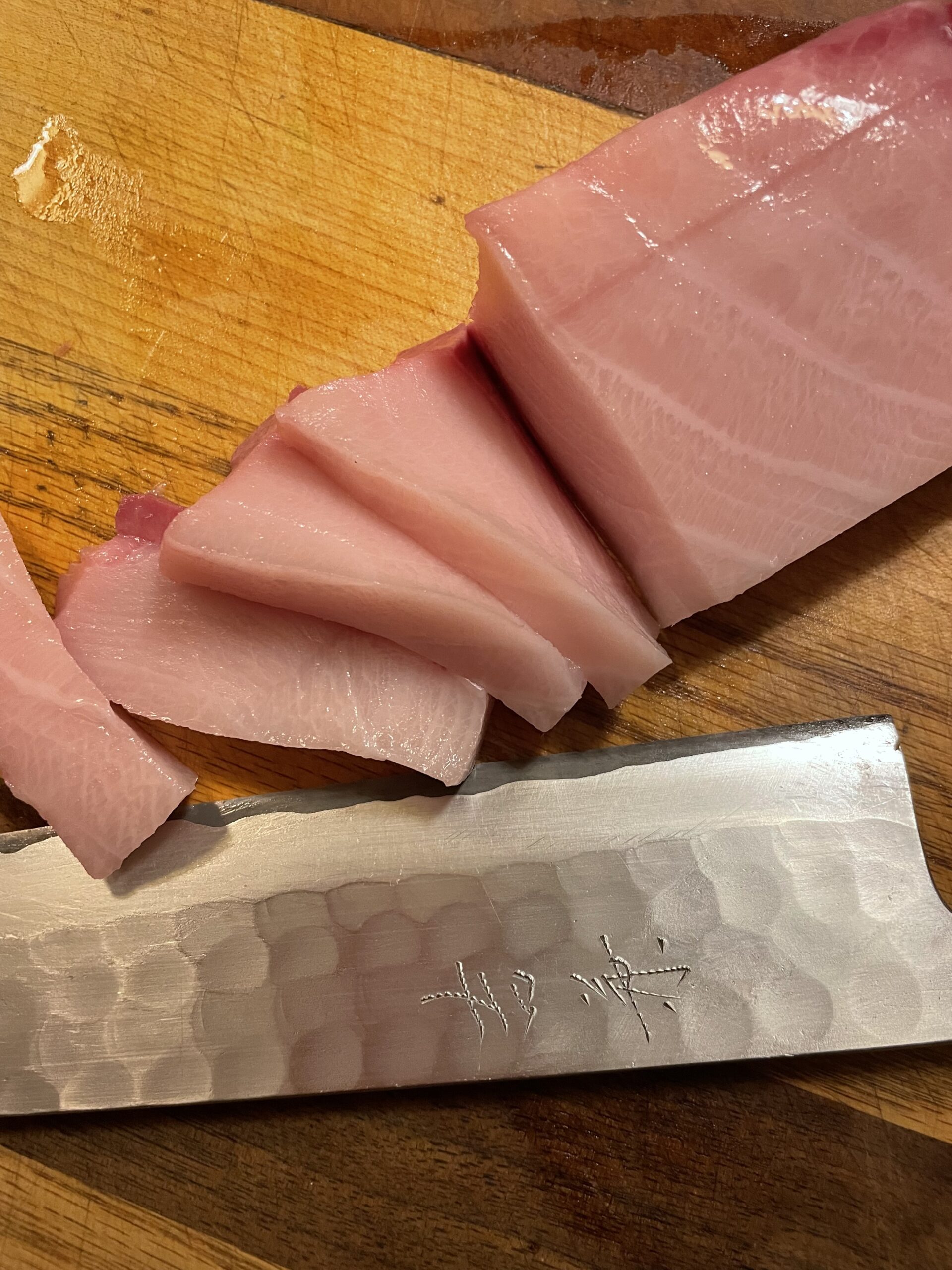 Pink fish sliced on cutting board with unique knife