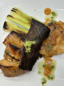 Miso-glazed black cod with crispy skin garnish and finger lime caviar, served with grilled yuca cake and charred leeks.